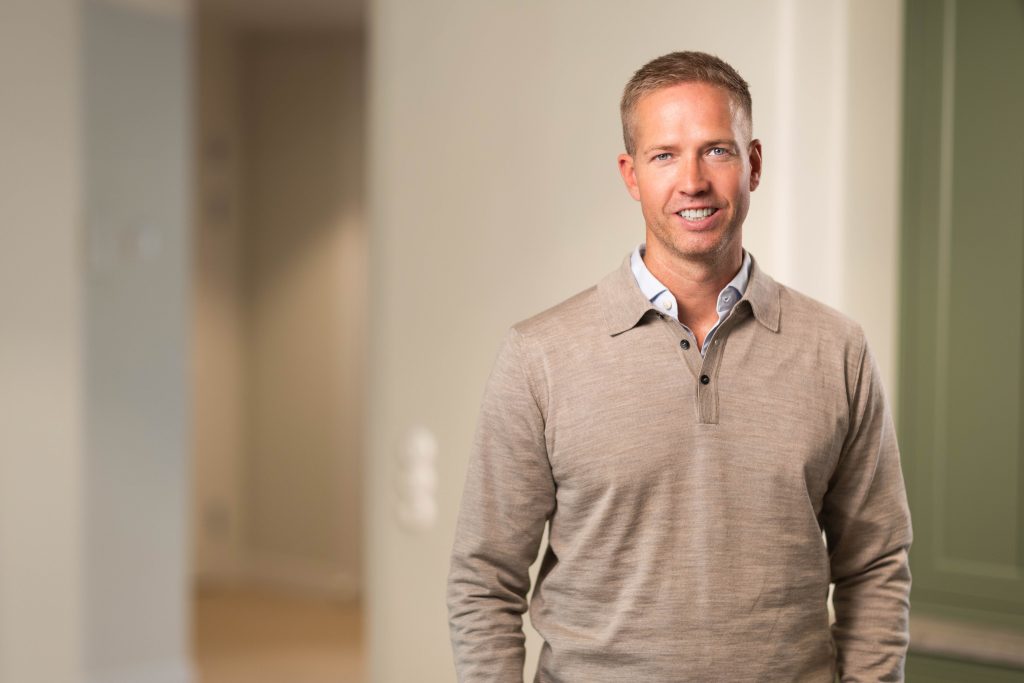 Man in beige sweater standing indoors.