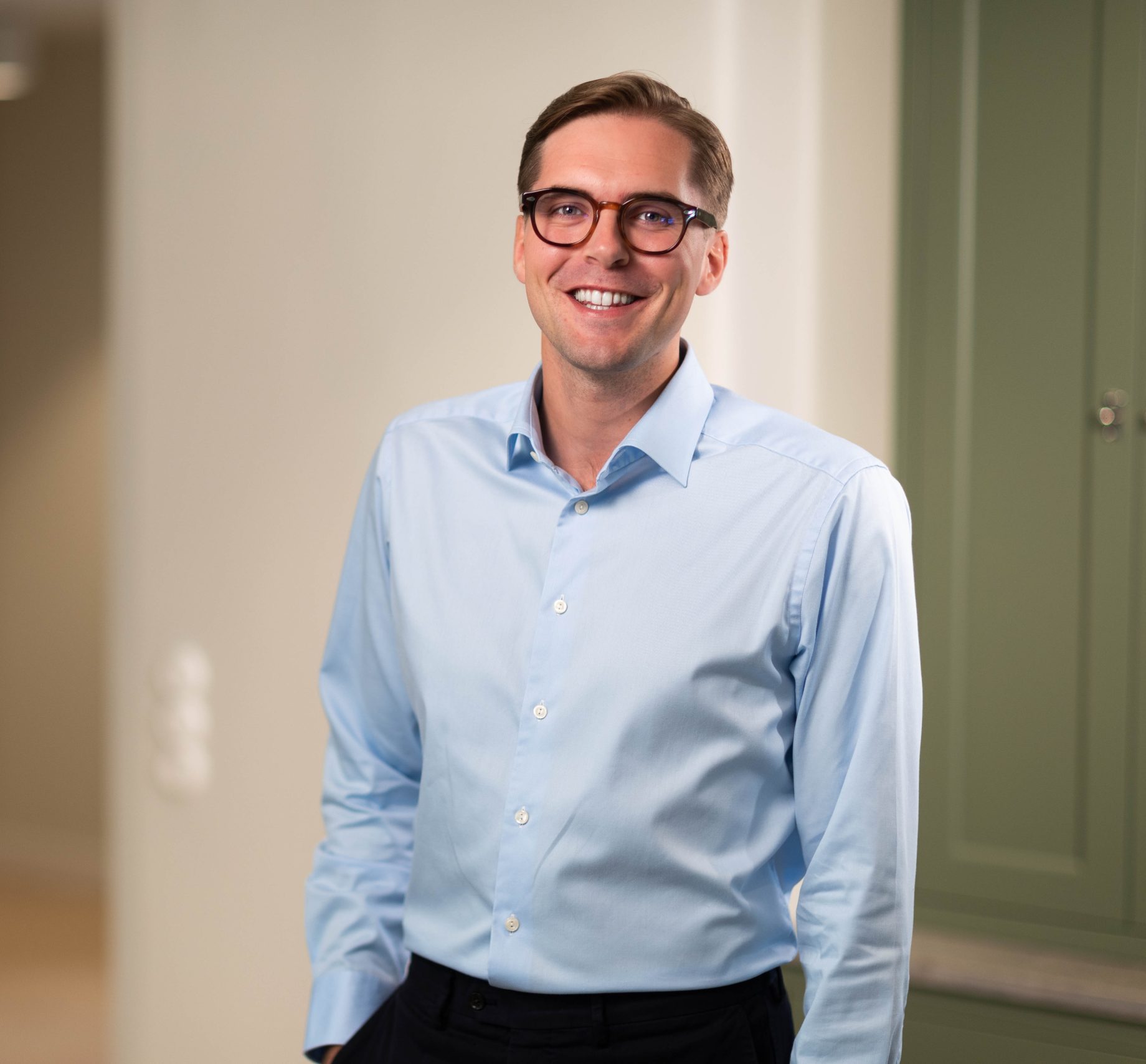 Man in light blue shirt and glasses smiling indoors.