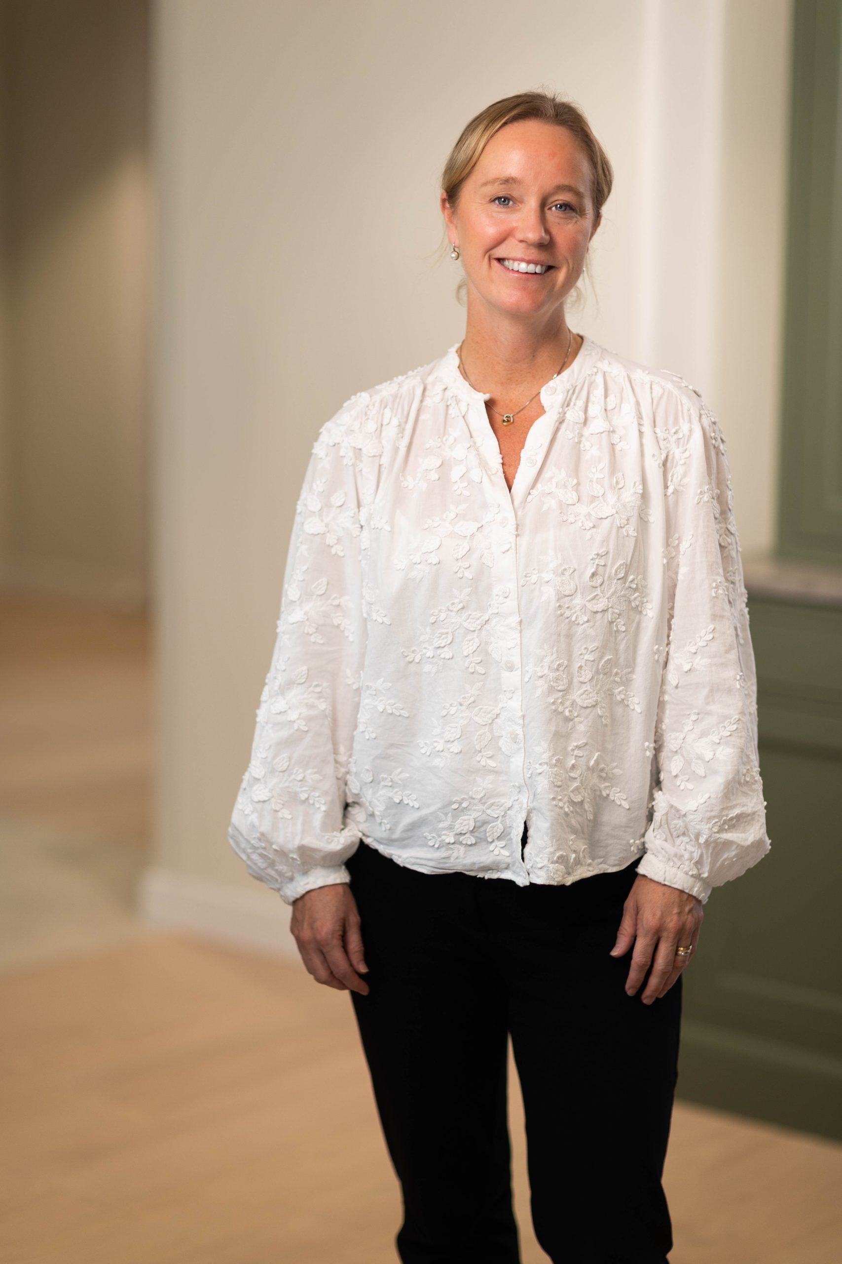 Woman in white blouse and black pants smiling indoors.