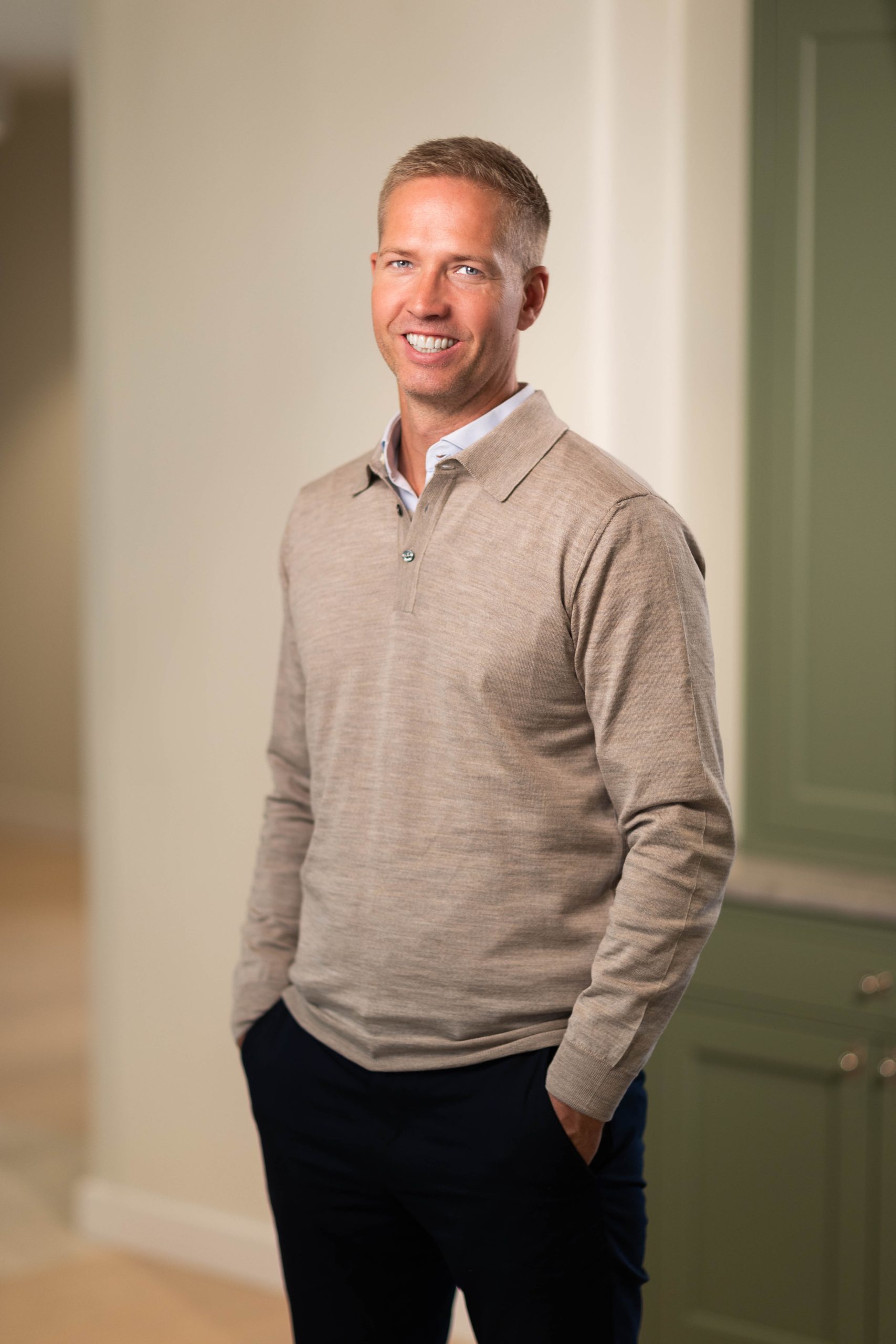 Man in beige sweater standing indoors.