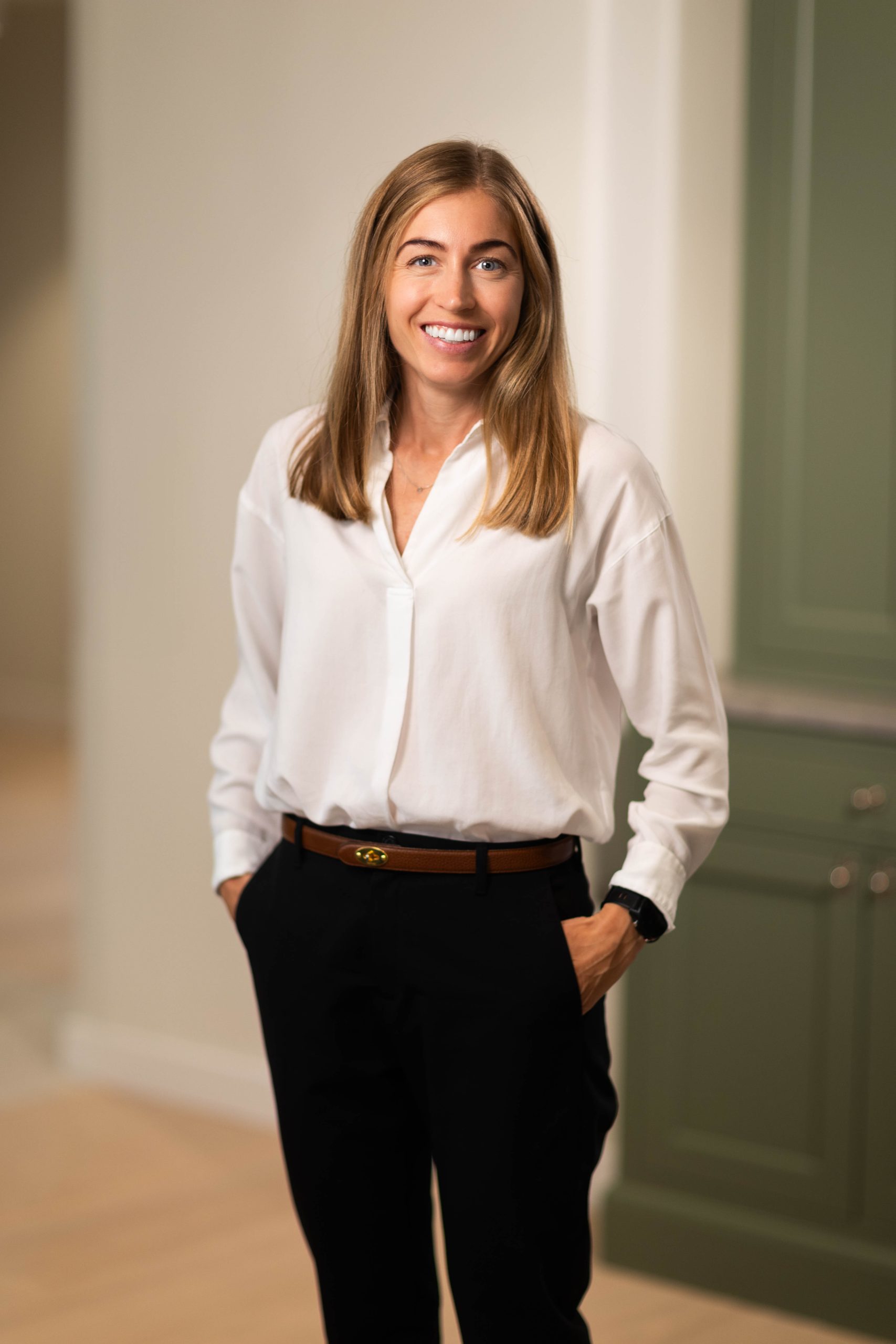Woman in white blouse and black pants smiling indoors.
